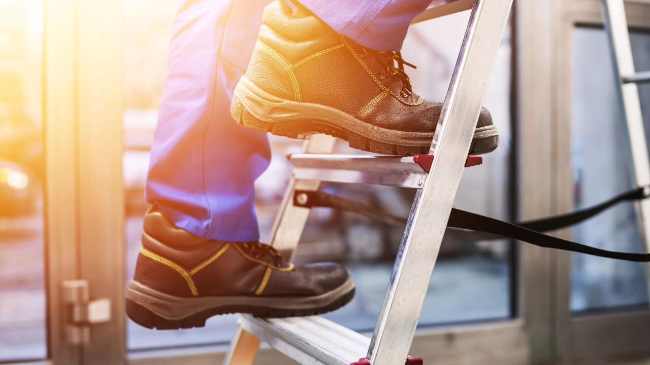 Arbeiter klettert mit Sicherheitsschuhen auf Leiter.